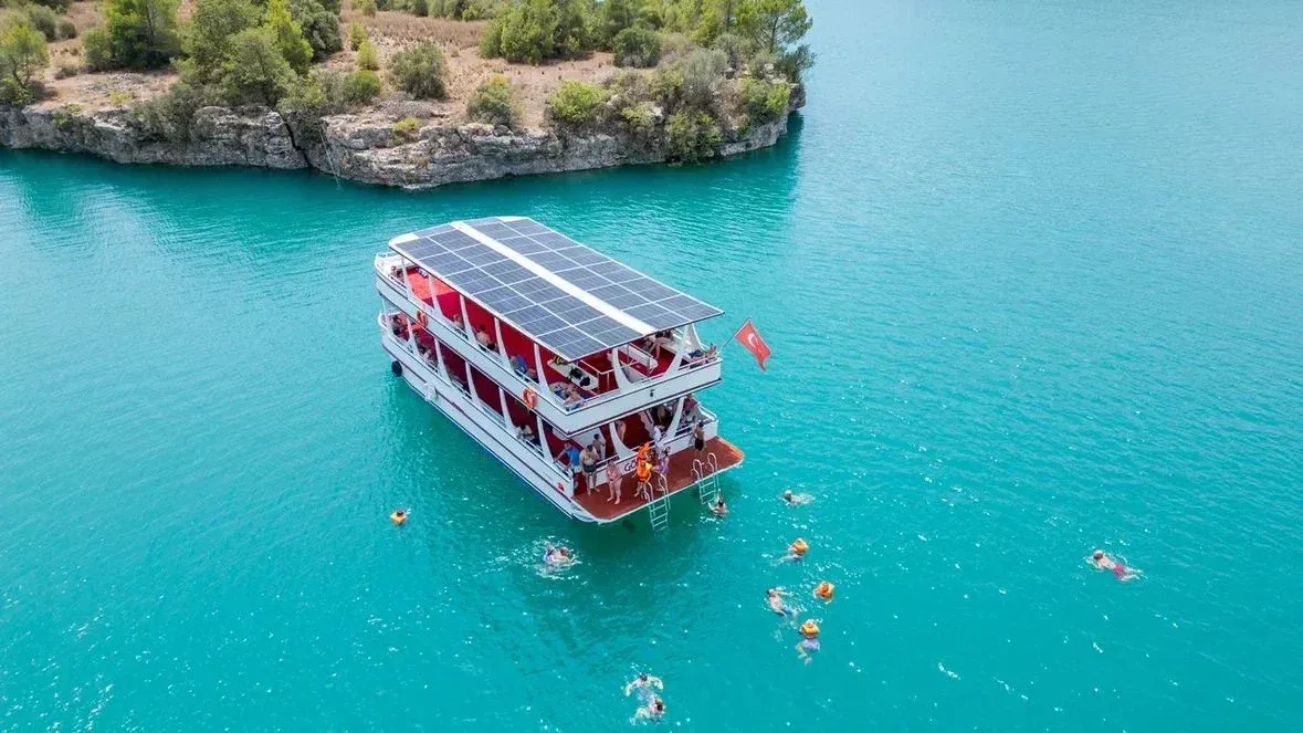 Swimmers around the platform of a double-deck boat on the turquoise water of the Oymapinar reservoir