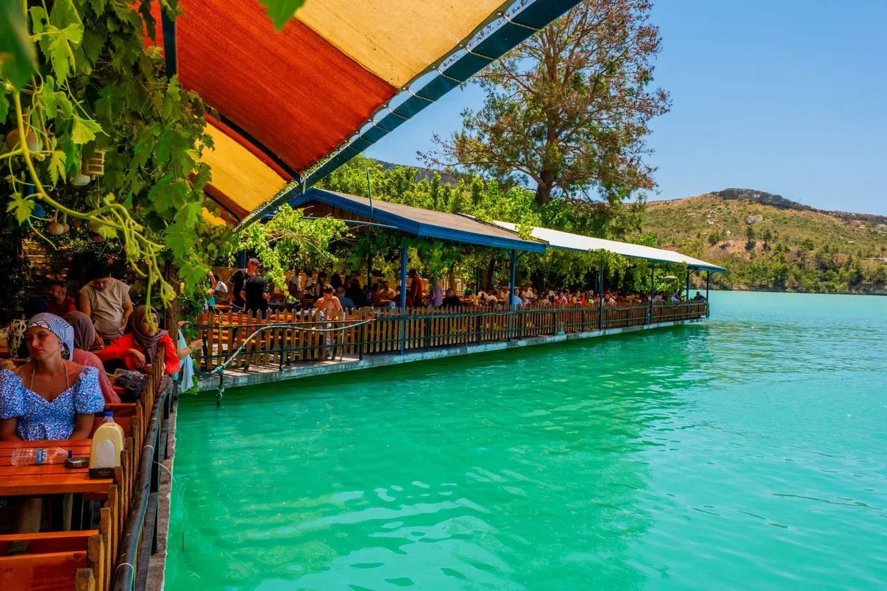 Lakeside restaurant terrace under orange awnings on the green water of Yeşilgöl, with bare hills behind