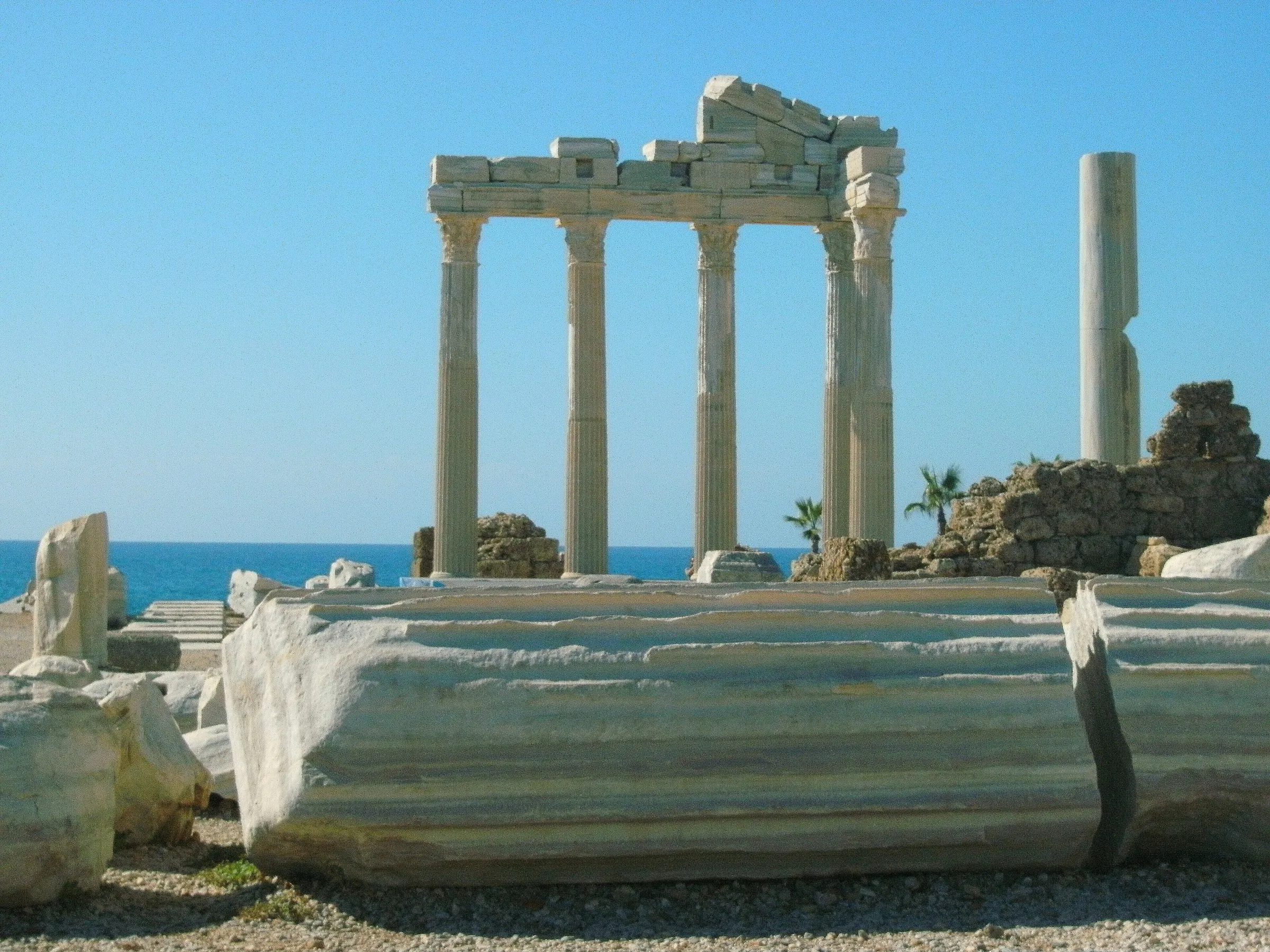 The four visible re-erected Corinthian columns of the Temple of Apollo on the headland at Side, a fallen column drum in the foreground and the sea behind